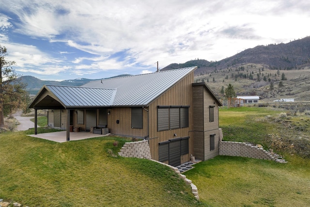 rear view of property featuring a patio, a standing seam roof, a yard, a mountain view, and metal roof