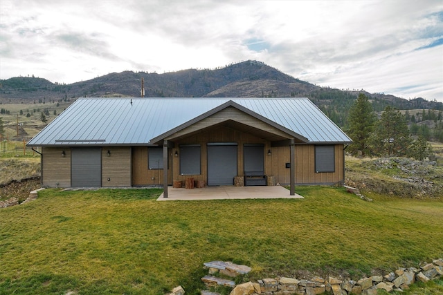 back of house with a standing seam roof, a patio area, a mountain view, and a lawn