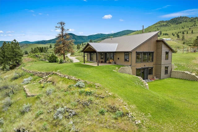 back of property featuring a patio area, a mountain view, metal roof, and a yard