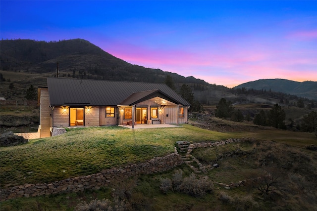 back of property at dusk with a patio area, a mountain view, metal roof, and a yard