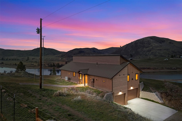 view of front of home with an attached garage, concrete driveway, a water and mountain view, and metal roof