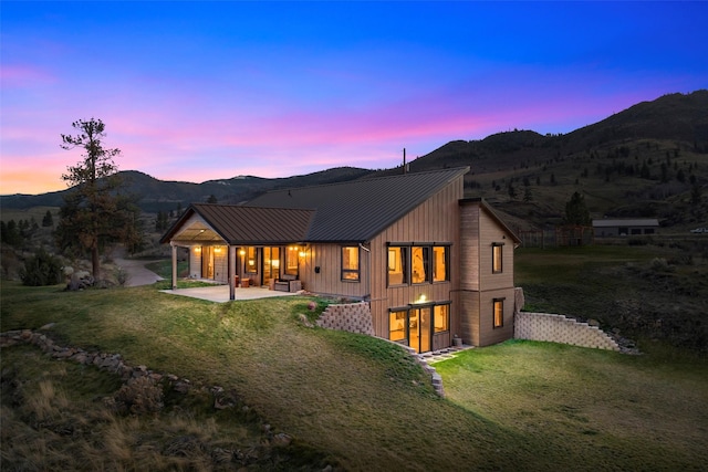 back of house featuring a lawn, a standing seam roof, a mountain view, metal roof, and a patio area