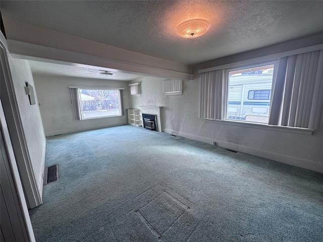 unfurnished living room with visible vents, a textured ceiling, a glass covered fireplace, carpet, and baseboards