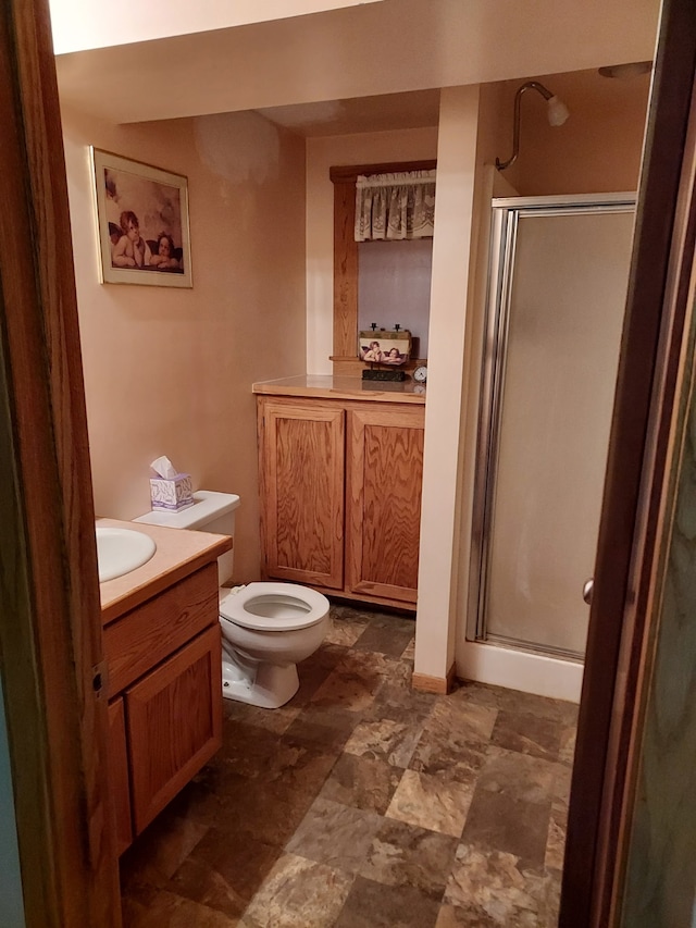 full bathroom featuring toilet, a stall shower, vanity, and stone finish floor