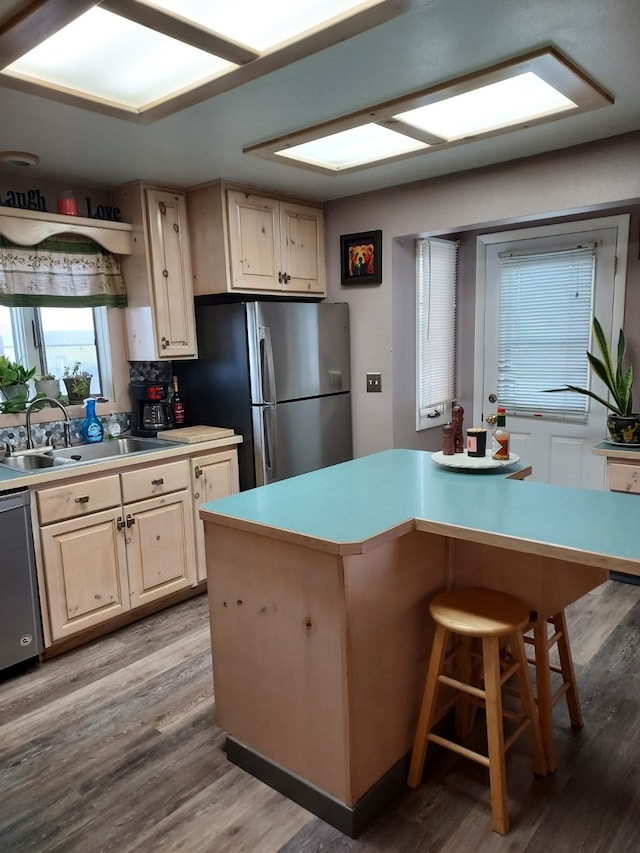 kitchen with light wood-type flooring, a sink, appliances with stainless steel finishes, a breakfast bar area, and light countertops