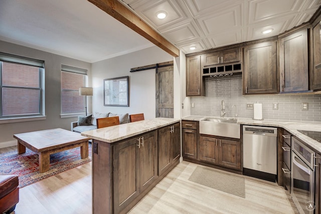 kitchen featuring a sink, tasteful backsplash, stainless steel appliances, a barn door, and light stone countertops