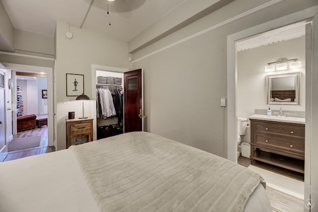 bedroom featuring a spacious closet, connected bathroom, wood finished floors, a closet, and a sink