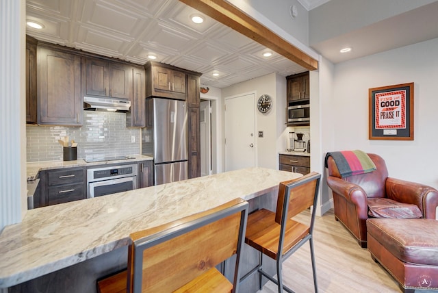 kitchen with under cabinet range hood, backsplash, appliances with stainless steel finishes, and a breakfast bar area