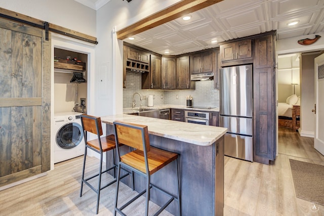 kitchen featuring under cabinet range hood, a sink, stainless steel appliances, a barn door, and washer / dryer