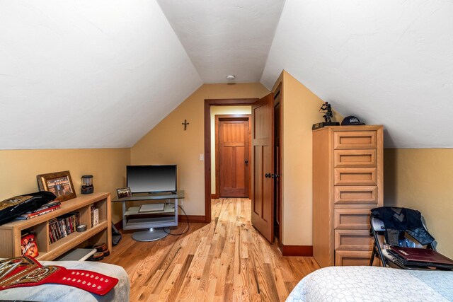 bedroom featuring baseboards, lofted ceiling, and light wood finished floors