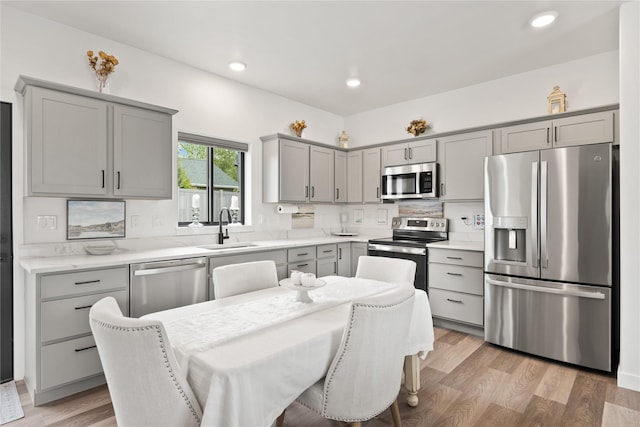 kitchen with a sink, gray cabinetry, light wood-type flooring, and stainless steel appliances