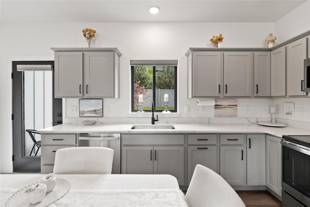 kitchen with gray cabinetry, light stone countertops, appliances with stainless steel finishes, and a sink