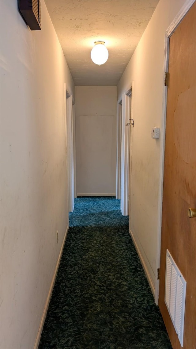 hallway featuring carpet flooring, a textured ceiling, baseboards, and visible vents