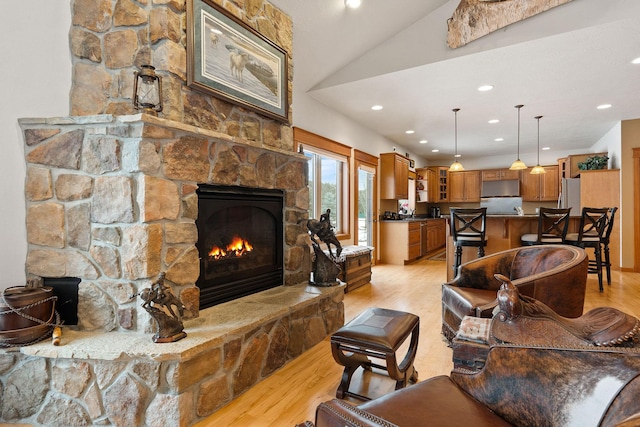 living area with recessed lighting, a stone fireplace, vaulted ceiling, and light wood finished floors