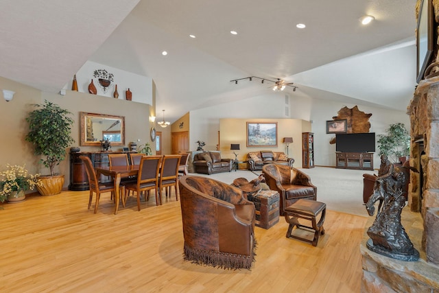 living area with a stone fireplace, vaulted ceiling, light wood-type flooring, and ceiling fan