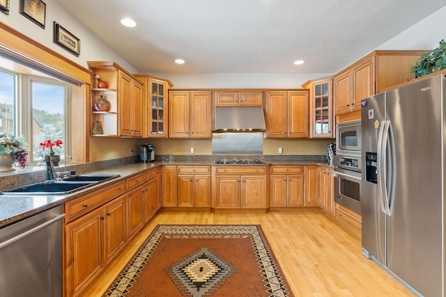 kitchen with brown cabinetry, a sink, stainless steel appliances, light wood-style floors, and under cabinet range hood