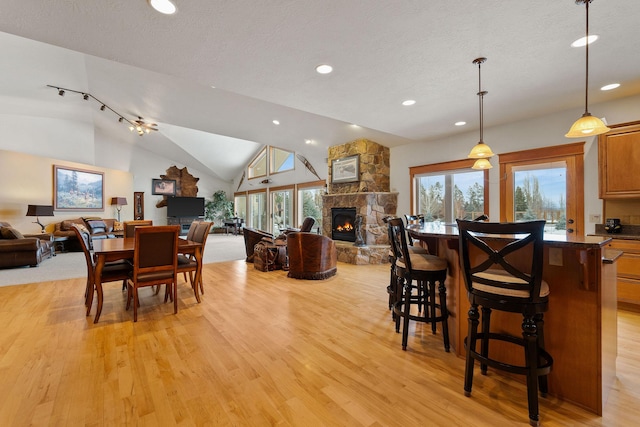 dining area with light wood-style flooring, a textured ceiling, recessed lighting, a stone fireplace, and lofted ceiling