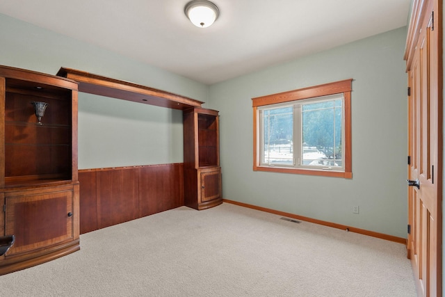 empty room with visible vents, baseboards, carpet, and a wainscoted wall