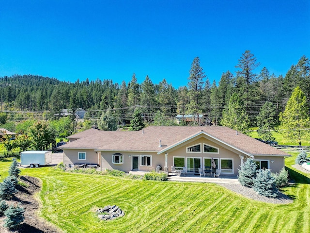 back of property featuring a yard, a patio area, and a forest view