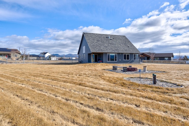back of house with an outdoor fire pit, roof with shingles, a yard, and fence