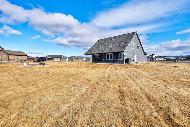 rear view of property featuring a yard, central air condition unit, and fence