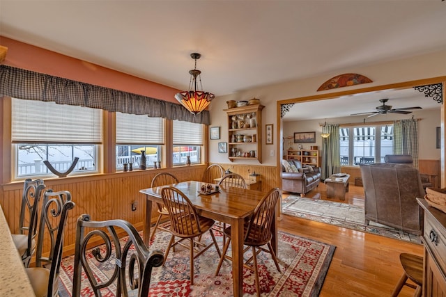 dining room featuring ceiling fan, wood finished floors, wood walls, and wainscoting