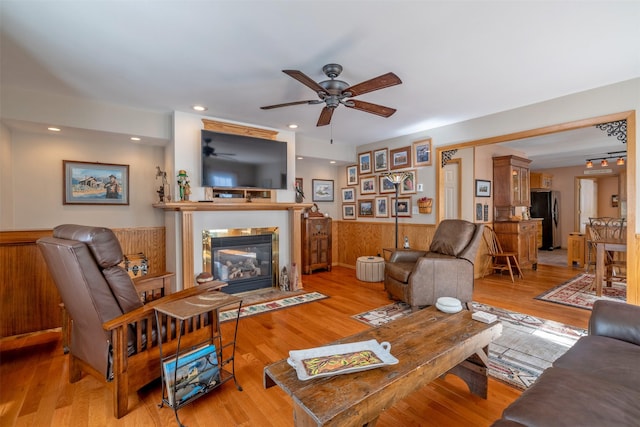 living area featuring a wainscoted wall, light wood-type flooring, recessed lighting, a tile fireplace, and a ceiling fan