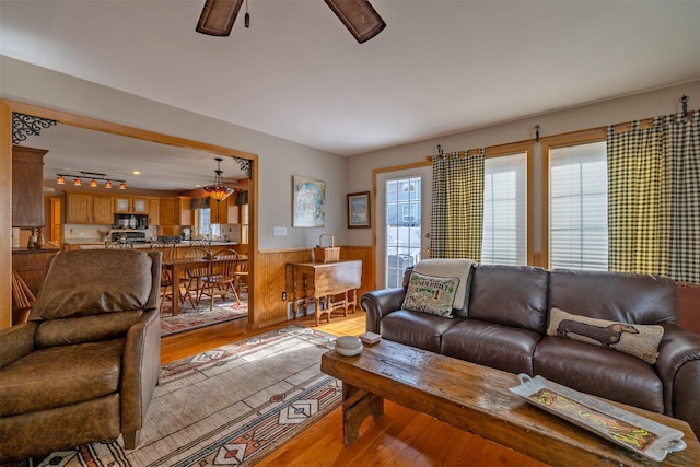 living area with a ceiling fan, wainscoting, and light wood finished floors