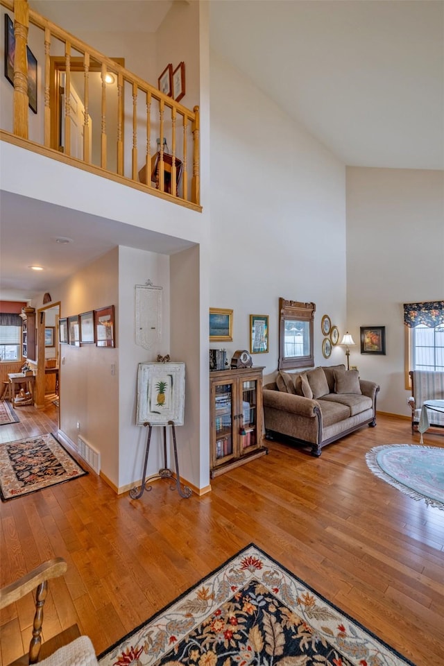 living area featuring hardwood / wood-style floors, a high ceiling, baseboards, and visible vents