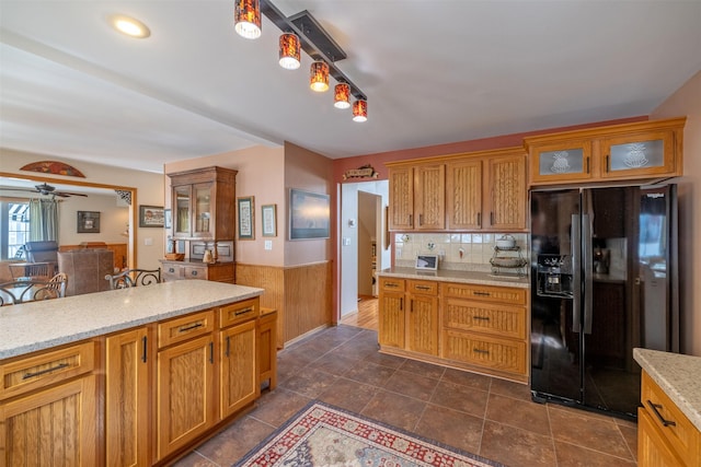 kitchen with light stone counters, ceiling fan, decorative backsplash, glass insert cabinets, and black fridge