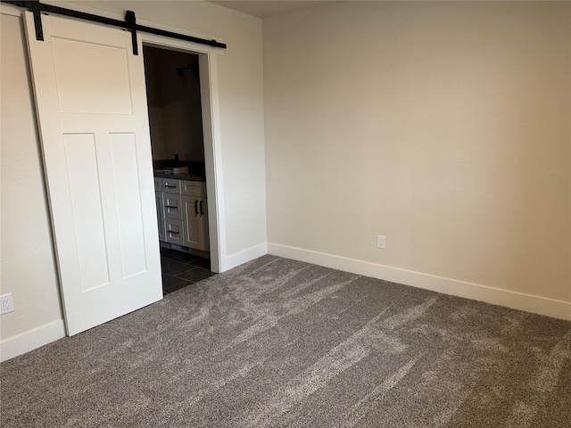 unfurnished bedroom with a barn door, baseboards, and dark colored carpet