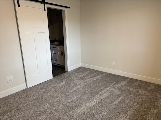 unfurnished bedroom with a barn door, baseboards, and dark colored carpet