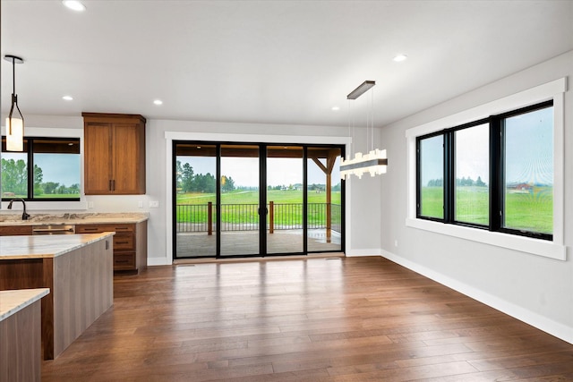 kitchen featuring light stone counters, decorative light fixtures, recessed lighting, brown cabinetry, and dark wood-style flooring