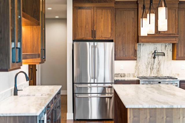 kitchen with brown cabinetry, light stone countertops, recessed lighting, freestanding refrigerator, and range