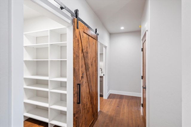 hall featuring dark wood finished floors, a barn door, recessed lighting, and baseboards