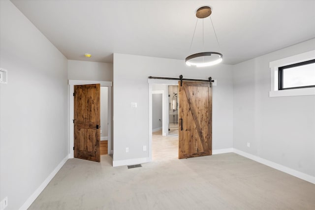 unfurnished bedroom featuring carpet flooring, visible vents, baseboards, and a barn door