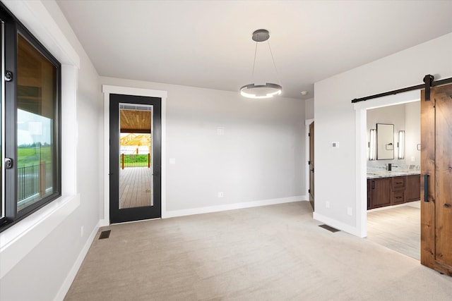 empty room with a barn door, light colored carpet, visible vents, and baseboards