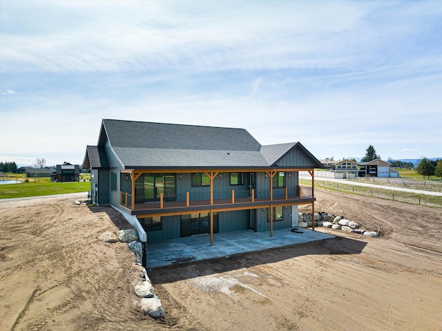 back of property featuring a carport, dirt driveway, a patio, and roof with shingles