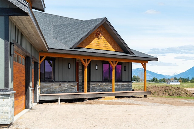 view of front of home featuring board and batten siding, a mountain view, stone siding, and a shingled roof