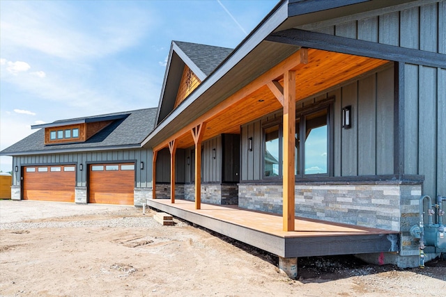 view of home's exterior with stone siding, board and batten siding, a shingled roof, and an attached garage