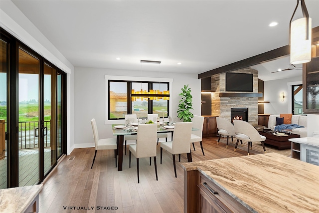 dining room featuring a stone fireplace, a healthy amount of sunlight, baseboards, and light wood-style floors