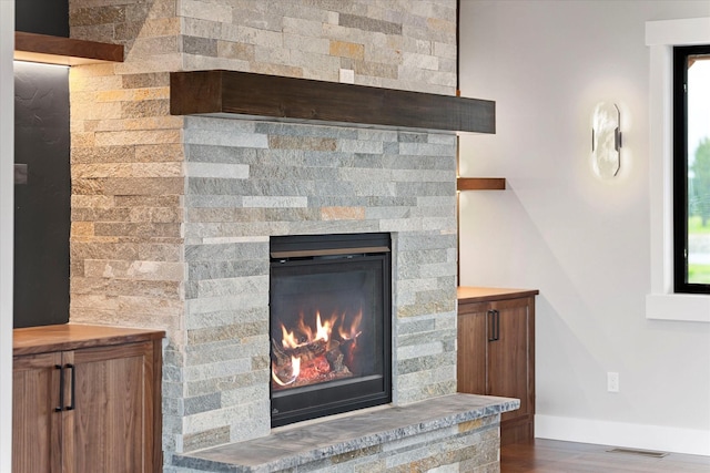 room details featuring a stone fireplace, visible vents, baseboards, and wood finished floors