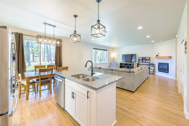 kitchen featuring light stone counters, light wood-style flooring, stainless steel appliances, and a sink