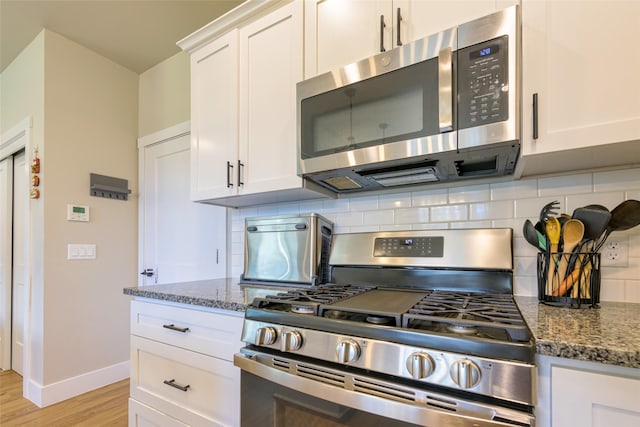 kitchen with decorative backsplash, stone counters, light wood-style flooring, stainless steel appliances, and white cabinetry