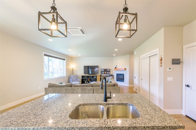 kitchen with a sink, decorative light fixtures, a glass covered fireplace, recessed lighting, and baseboards