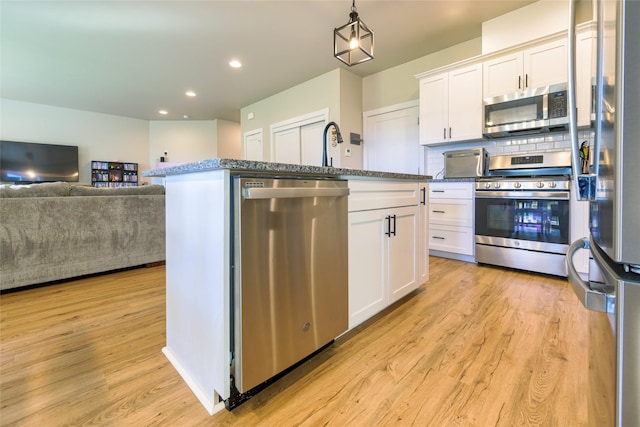 kitchen featuring light wood finished floors, stainless steel appliances, white cabinets, open floor plan, and backsplash