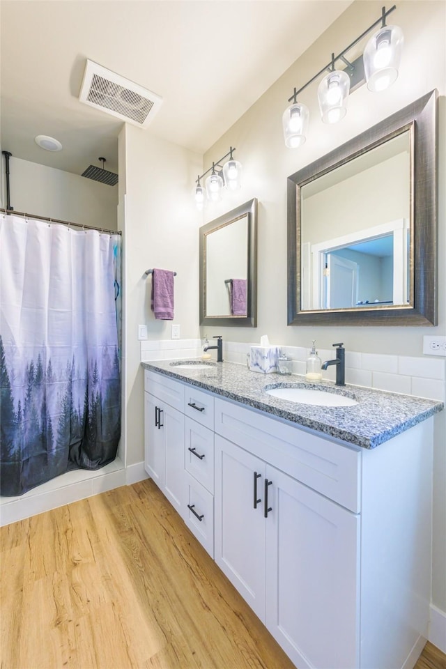 bathroom featuring a sink, visible vents, wood finished floors, and double vanity