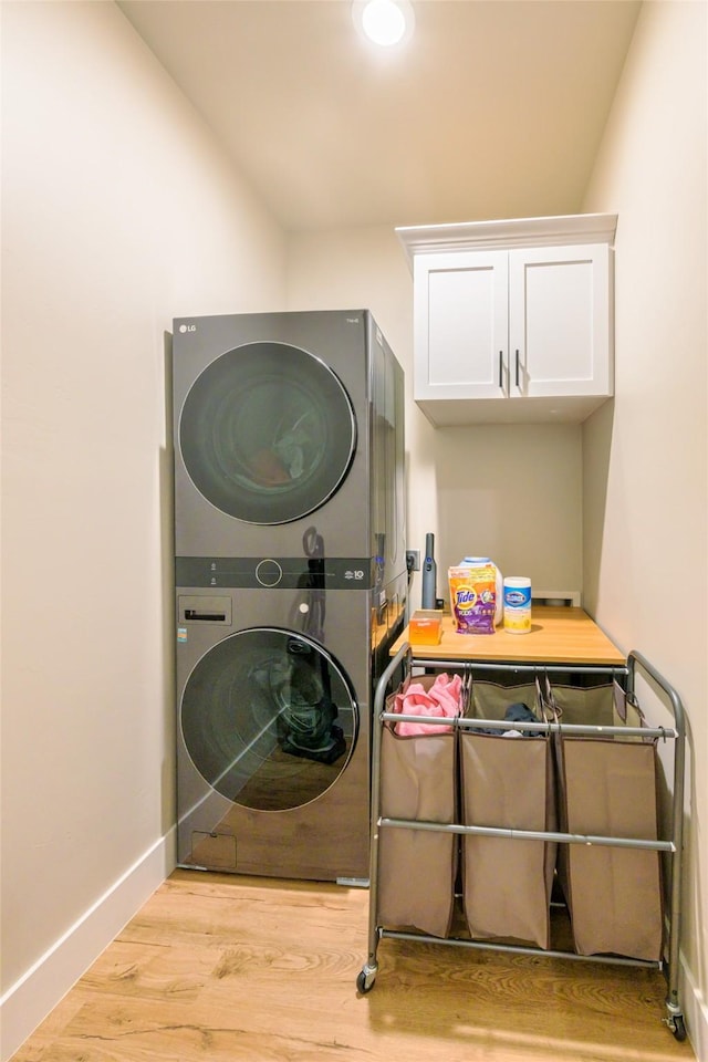 laundry room with cabinet space, baseboards, wood finished floors, and stacked washer / dryer