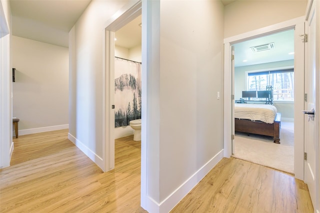 corridor with light wood-type flooring, visible vents, and baseboards