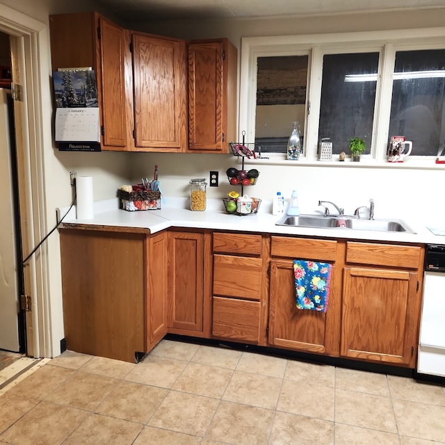 kitchen with brown cabinets, a sink, light tile patterned flooring, white dishwasher, and light countertops